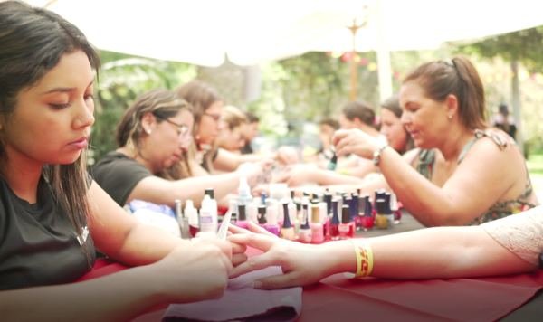 Manicuristas atendiendo a varias personas en una mesa durante un evento